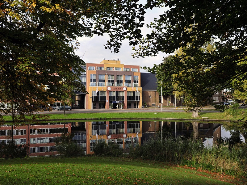 Amrâth Hotel Alkmaar with colorful facades and reflection in the water, surrounded by greenery.