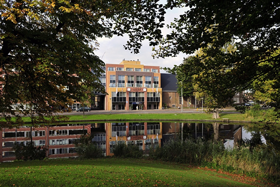 Amrâth Hotel Alkmaar with colorful facades and reflection in the water, surrounded by greenery.