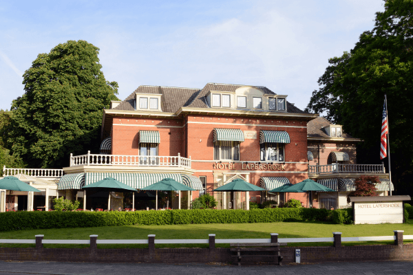 Front view of Amrâth Hotel Lapershoek Arenapark in Hilversum, a stately villa with a terrace surrounded by greenery.