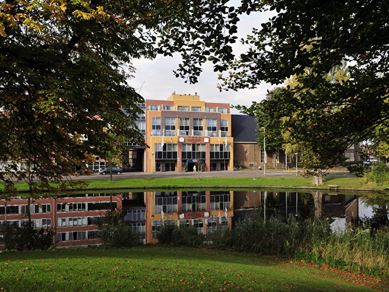 Amrâth Hotel Alkmaar met kleurrijke gevels en reflectie in het water, omringd door groen.