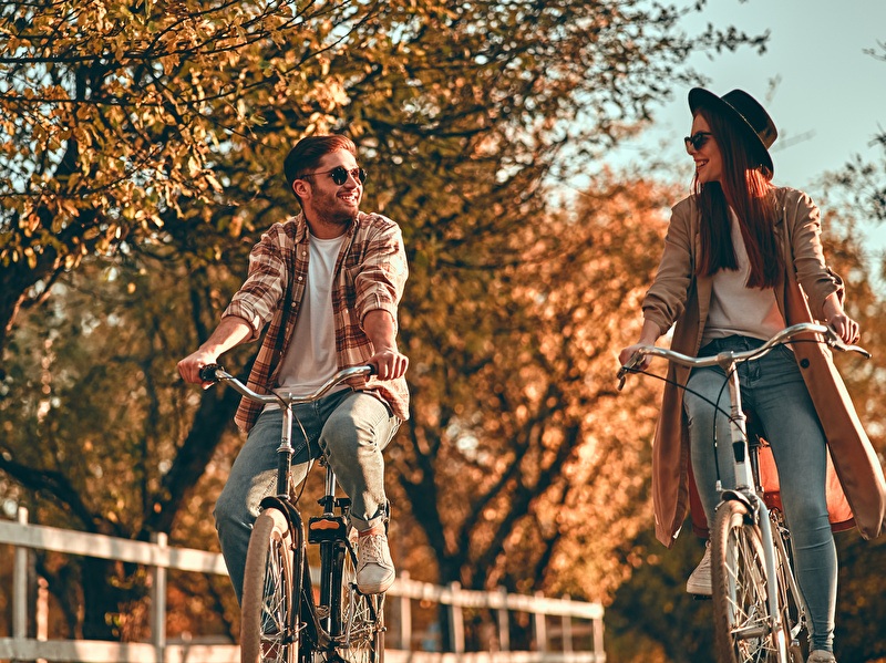 Man en vrouw fietsen lachend naast elkaar op een zonnige herfstdag.