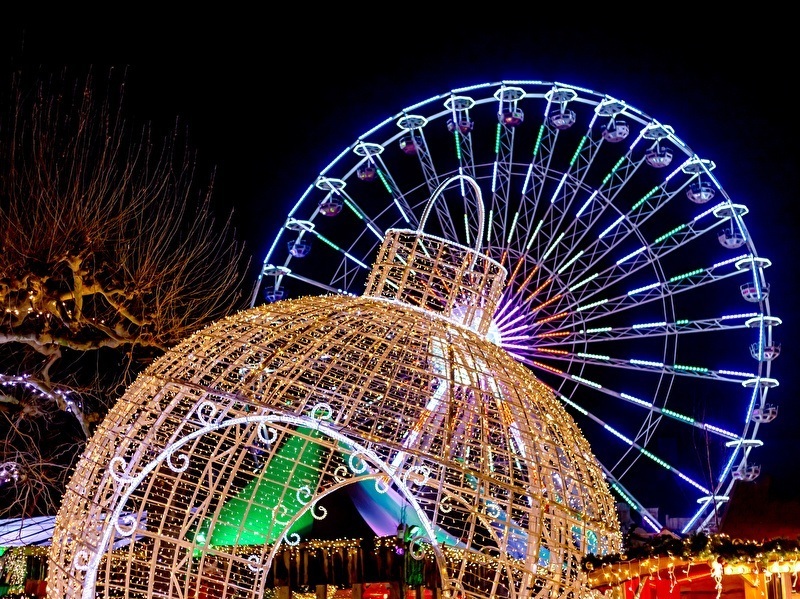 Verlichte kerstdecoraties en een grote reuzenrad ’s avonds tijdens een winterevenement, met kleurrijke lampjes en feestelijke sfeer