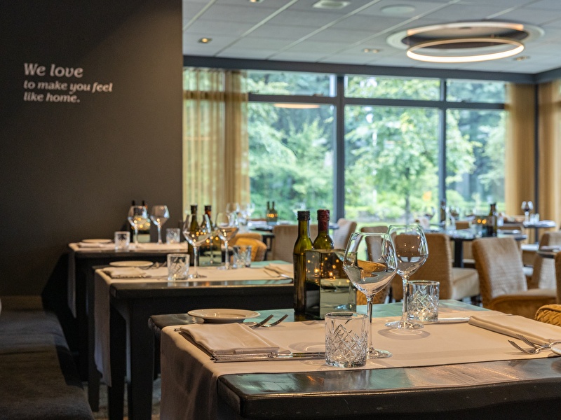 Modern restaurantinterieur van Amrâth Berghotel Amersfoort met uitzicht op het groen en sfeervol gedekte tafels.