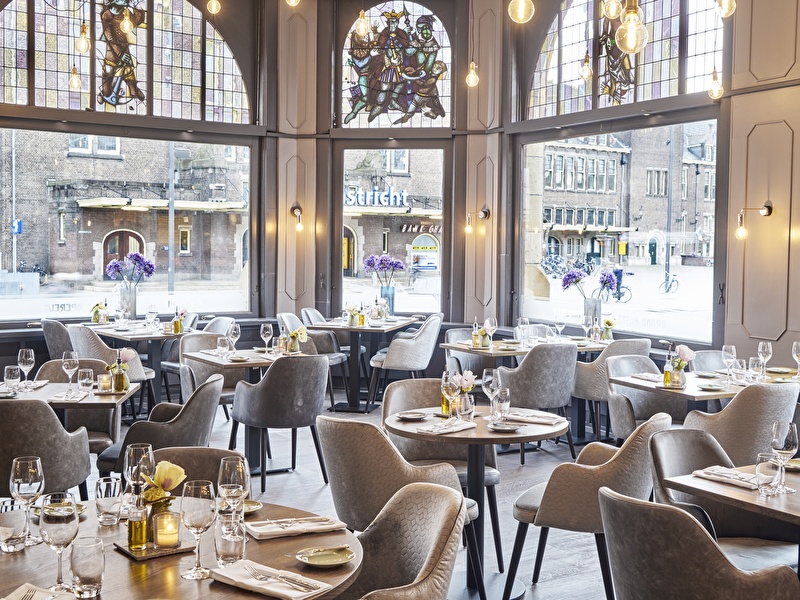 Sfeervol restaurant met grote glas-in-loodramen in Amrâth Grand Hotel de l’Empereur, gedekt voor lunch of diner.