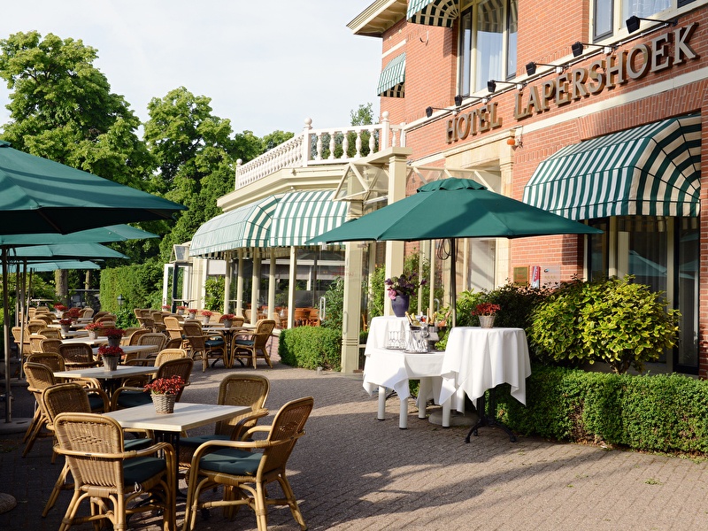 Zonnig terras met rieten stoelen en groene parasols bij Amrâth Hotel Lapershoek Arenapark in Hilversum.