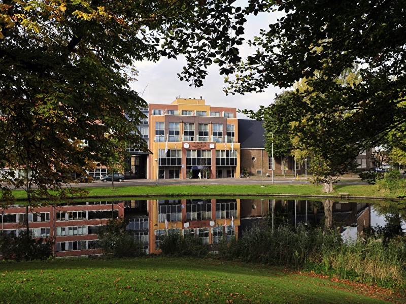Amrâth Hotel Alkmaar met kleurrijke gevels en reflectie in het water, omringd door groen.