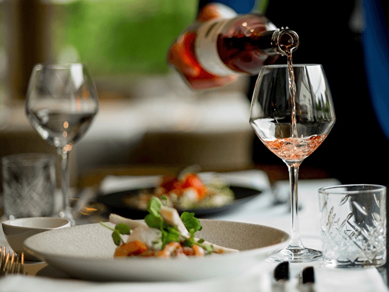 Ein Glas Rosé wird an einem stilvoll gedeckten Tisch in einem Restaurant eingeschenkt, mit raffinierten Gerichten auf eleganten Tellern.