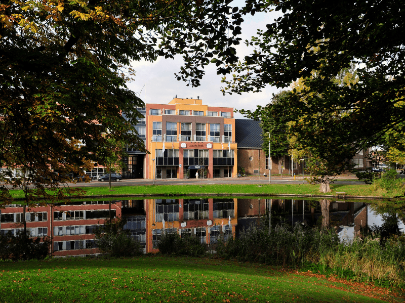 Amrâth Hotel Alkmaar met kleurrijke gevels en reflectie in het water, omringd door groen.