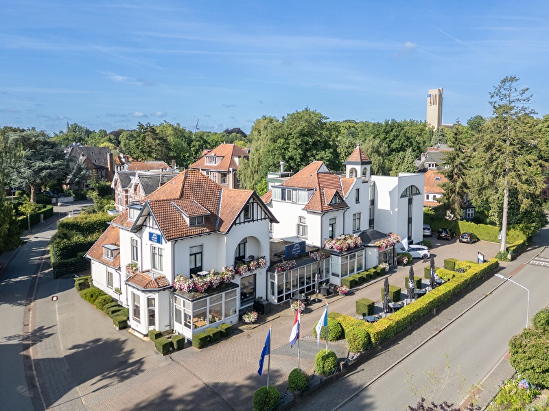 Amrâth Hotel Media Park in Hilversum, lichte gevel met kleurrijke bloemen en buitenzitplaatsen.