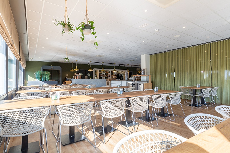 Modern en licht restaurant van Amrâth Airport Hotel Rotterdam met houten tafels, gevlochten stoelen en een open bar met messing hanglampen.