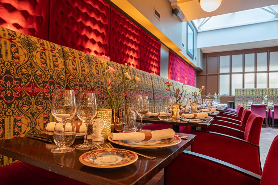 Restaurant Seven Seas in Grand Hotel Amrâth Amsterdam met een bruine houten tafels met rode fluwelen stoelen opgedekt met gekleurd servies, servetten en wijnglazen
