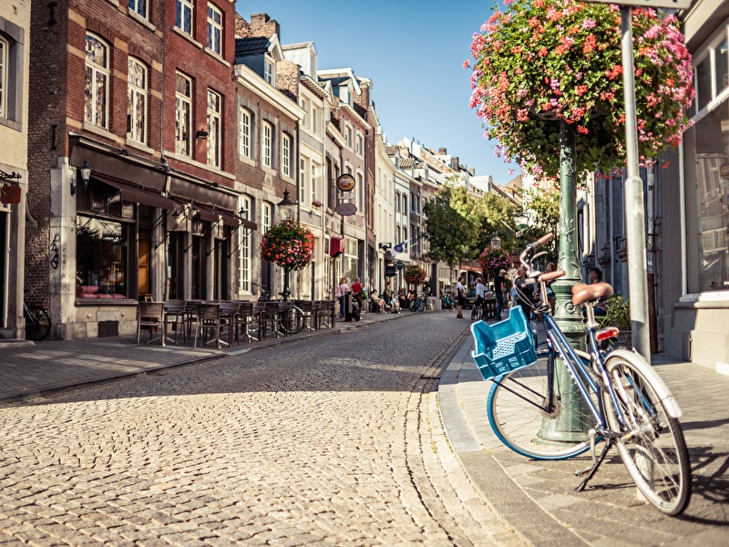 Atmospheric street in the center of Maastricht with historic facades, terraces, and a bicycle with a blue crate against a lamppost, on a sunny day.