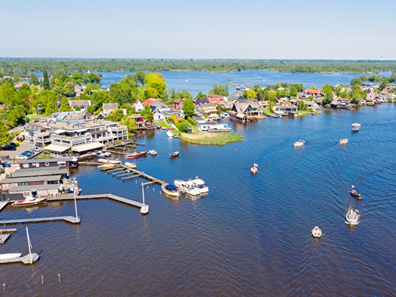 Aerial photo of the Loosdrechtse Plassen with sailing boats, houses by the water, and green nature surrounding it, on a glorious summer day.