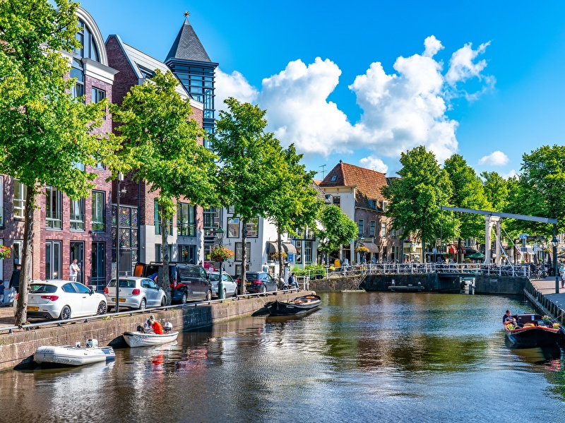 Summer day in Alkmaar with boats on the canal, green trees, historical buildings, and a white drawbridge under a blue sky with clouds.