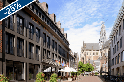 Amrâth Grand Hotel Frans Hals is located on a street with a church and building in the background, surrounded by trees and a clear sky.