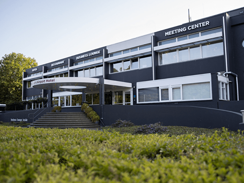 Vooraanzicht van Amrâth Airport Hotel Rotterdam met entree, trap en duidelijke borden voor hotel, restaurant en meeting center.