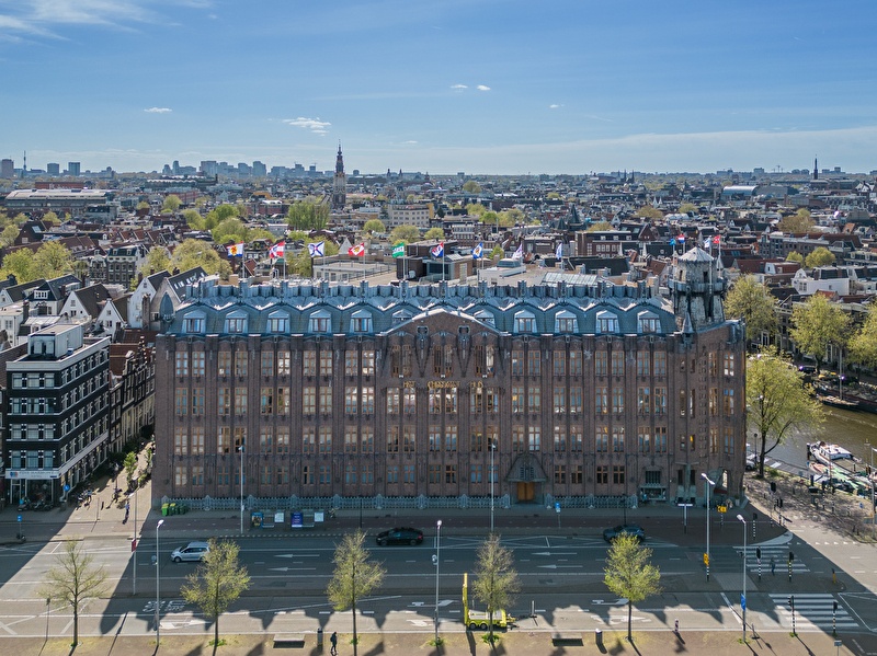 Luchtfoto van Grand Hotel Amrâth Amsterdam, een imposant art-nouveaugebouw aan het water, met uitzicht over de stad.