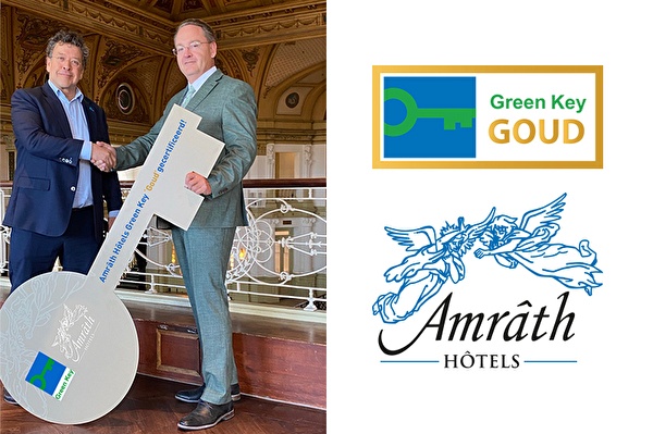 Twee mannen schudden handen bij overhandiging van een grote symbolische sleutel met Green Key-logo, binnen in een sierlijke ruimte. Rechts het Green Key Goud-logo en het Amrâth Hôtels-logo.